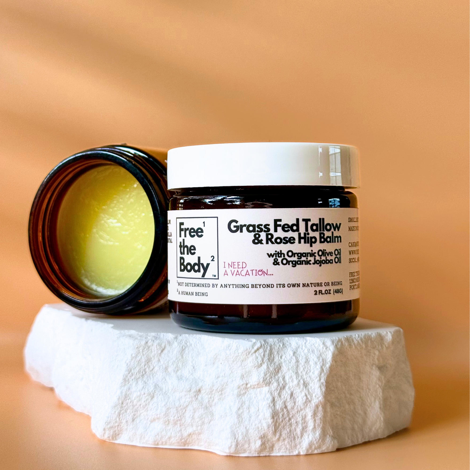 Free the Body Grass Fed Tallow & Rose Hip Balm jar on a stone surface with a beige background