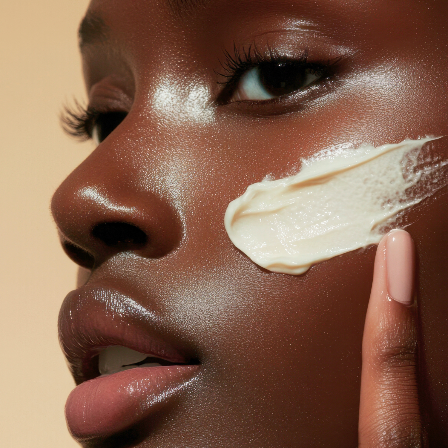 Close-up of a woman's face with cream applied to her cheek against a beige background
