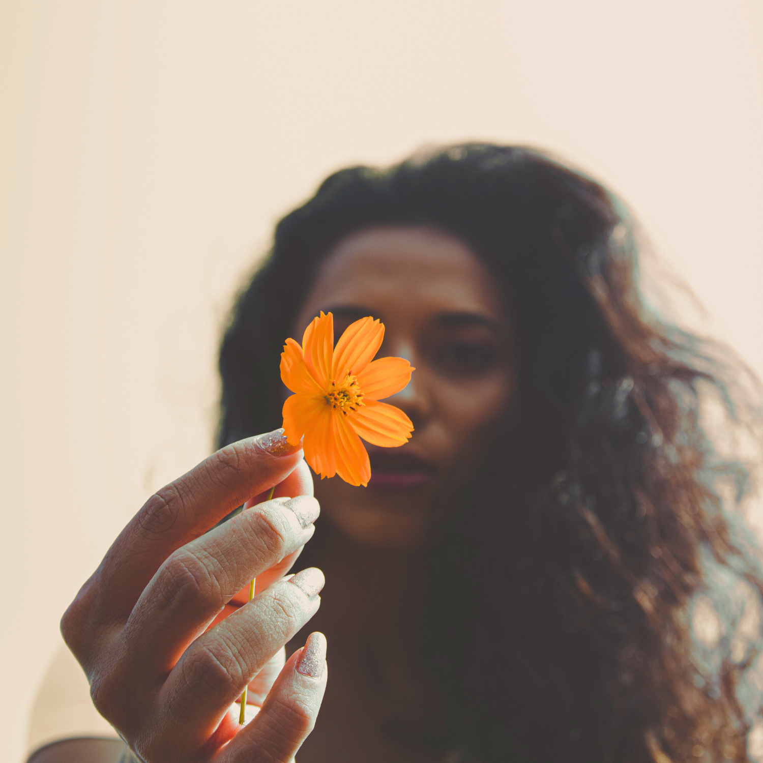 Woman holding an orange flower in front of her face with a blurred background
