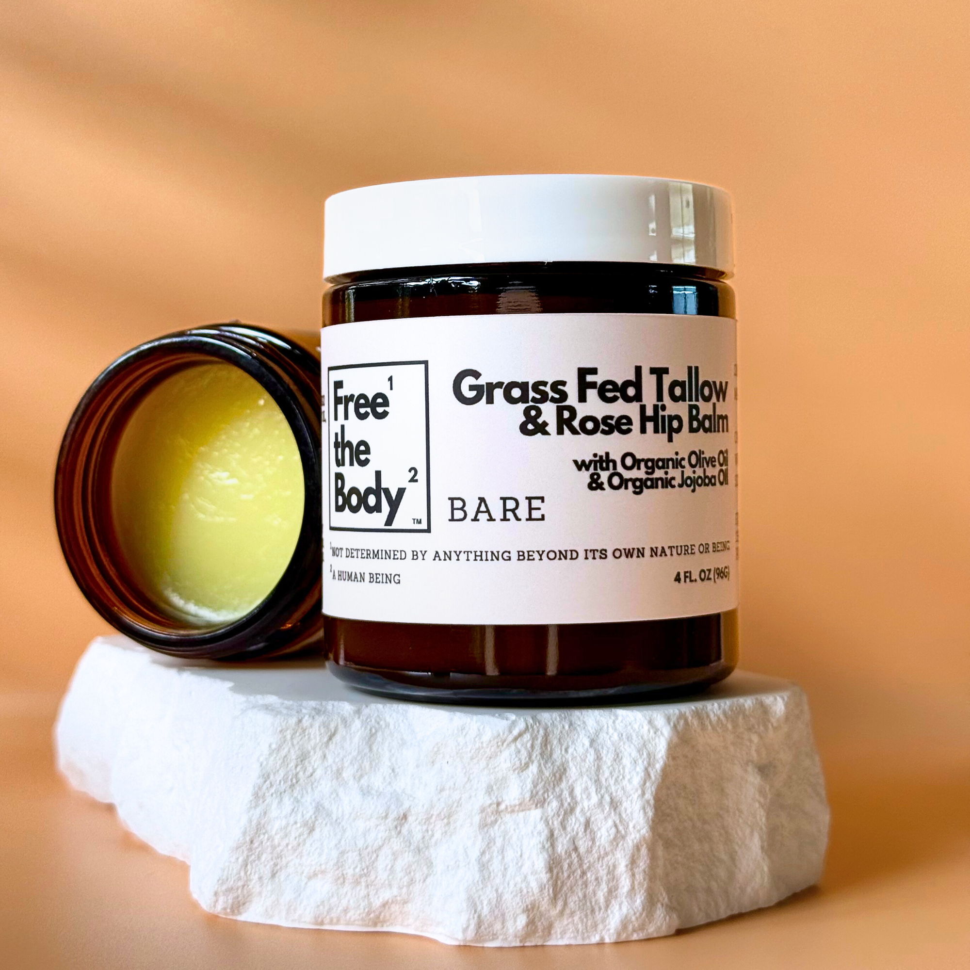 Balm jar with open lid on a stone surface against an orange background